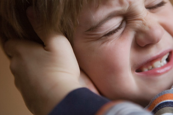 niño mostrando dolor en su oído, su mano sujeta su oído fuertemente